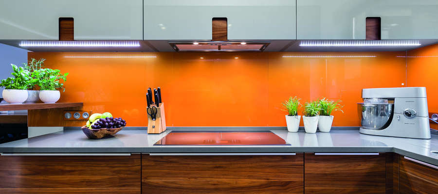 Pomarańczowe szkło nad blatem kuchennych świetnie wpisuje się w nowoczesną kuchnię.