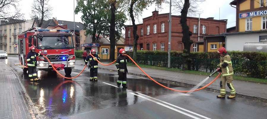 Strażacy-ochotnicy usuwaja plamę ropopochodną z jezdni w centrum Susza