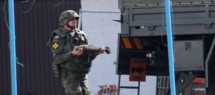 Żołnierz z jednostki w Braniewie przenosi niewybuch do specjalnego samochodu.
