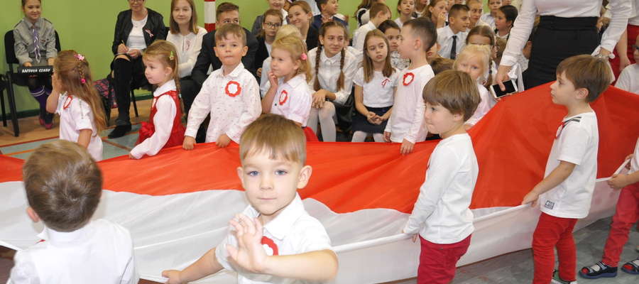 Przedszkolaki w biało - czerwonych strojach nieśli  trzydziestometrową flagą narodową