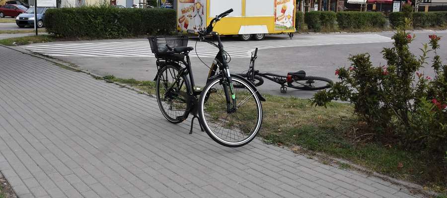 Rower stojący na chodniku i rower lezący na parkingu w miejscu zdarzenia z udziałem rowerzystów w Działdowie