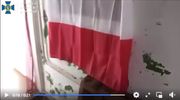 Skuci mężczyźni leżą na ziemi. Na ścianie wisi polska flaga